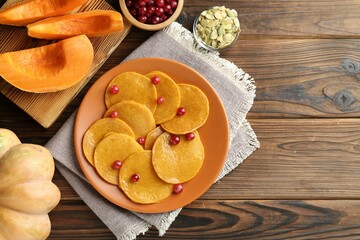 Tasty pumpkin pancakes with cranberries served on wooden table, flat lay. Space for text