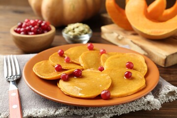 Tasty pumpkin pancakes with cranberries served on wooden table, closeup