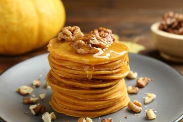 Tasty pumpkin pancakes with honey and walnuts on table, closeup