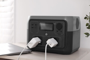 Laptop charging from portable power station on wooden table indoors