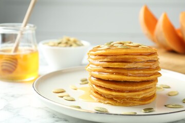Tasty pumpkin pancakes with seeds on white marble table, closeup