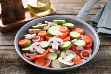 Frying pan with mix of fresh vegetables and mushrooms on wooden table, closeup