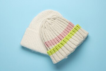 Warm woolen hats on light blue background, top view