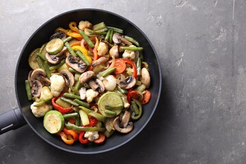 Different vegetables and mushrooms in frying pan on grey table, top view. Space for text