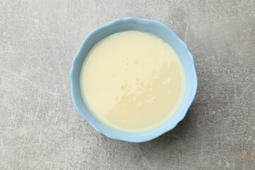 Condensed milk in bowl on light grey table, top view