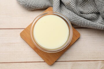Condensed milk in bowl on light wooden table, top view