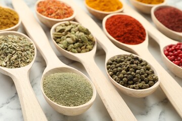 Different aromatic spices in spoons on white marble table, closeup
