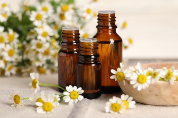 Bottles of essential oil and chamomile flowers on table, closeup