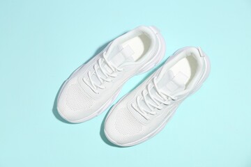 Pair of stylish white sneakers on light blue background, top view