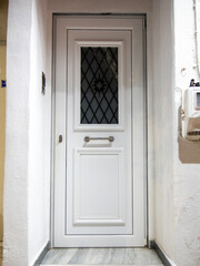 A white entrance door features a diamond-patterned glass panel. It is framed by light-colored walls and tiled flooring, enhancing the welcoming ambiance of the hallway.