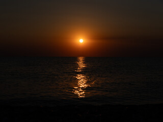 A vibrant sunset casts orange and gold hues across the ocean, reflecting beautifully on the water. The peaceful scene evokes relaxation and tranquility at the shore.