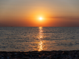 A breathtaking sunset unfolds over the ocean, illuminating the horizon with warm hues. The calm water mirrors the vibrant colors, creating a peaceful atmosphere perfect for reflection.