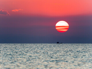 The sun sets on the horizon, casting vibrant oranges and pinks across the sky and reflecting on the calm ocean waters.
