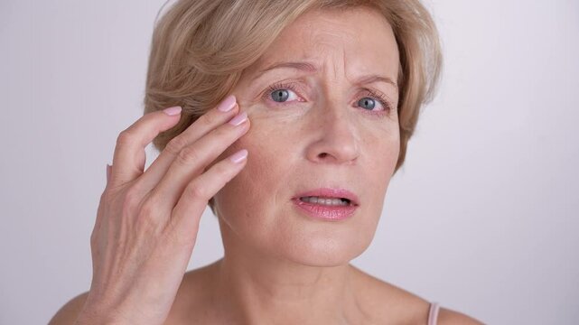 A youthful mature blond woman looking at the mirror at her aging skin, upset by wrinkles and flaws. Natural beauty, graceful aging