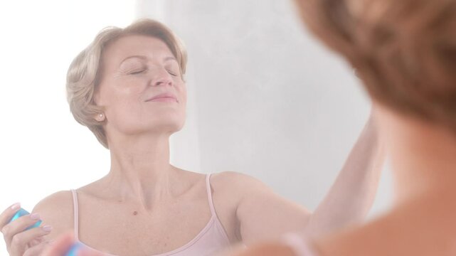 A sophisticated mature woman in her 50s enjoys spraying hydrating mist for face. Graceful selfcare and natural beauty