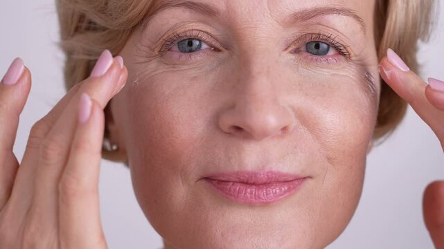 Portrait of naturally beautiful middle-aged woman looking at camera, applying night cream and finger-tapping her face. Self-care rituals