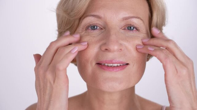 Positive beautiful aging lady takes care of her skin, finger-tapping anti-aging skincare products. Selflove, confidence, inner strength