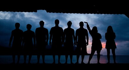 Silhouette of lined up friends staring at beautiful ocean at dusk
