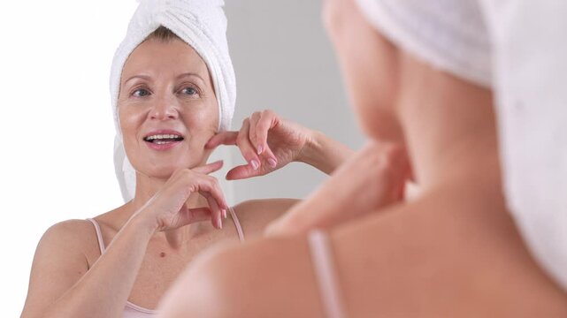 A graceful and mature woman in her 50s is joyfully touching her face, embracing the beauty of aging and her beloved skincare routines