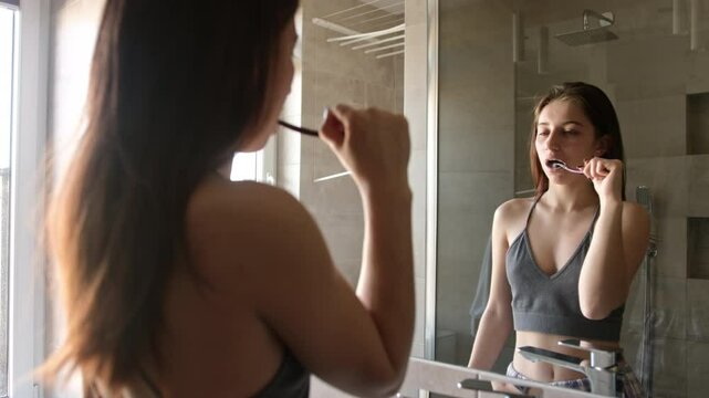 Girl Brushing Her Teeth In The Bathroom While Looking In The Mirror