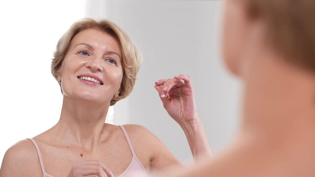 A mature woman reflects on her beauty looking at the mirror, celebrating the grace of aging while embracing selflove and skincare. Slo mo