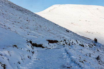 Hikers descending Pen-y-Fan in the Brecon Beacons during a cold, snowy winter