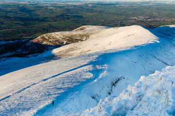 Lone hiker descending a snow covered mountain ridge in the late afternoon