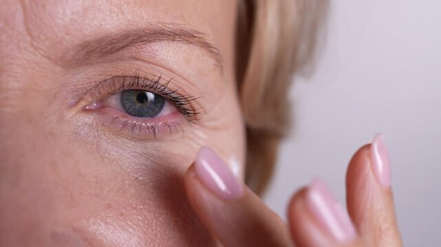 Extreme close up shot of mature female finger-tapping eye cream. Beautiful aging woman enjoying morning skincare routine. 4k high res