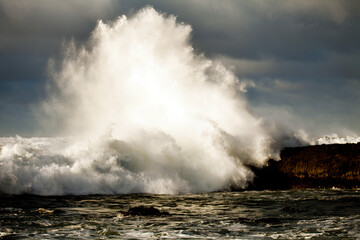 Glowing ocean wave crashing over rocky island patch