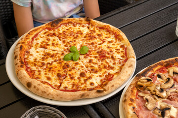 Close-up of Margherita pizza on a restaurant table with basil garnish, delicious authentic Italian cuisine, wood-fired pizza, dining outdoors, food photography, one person, classy casual setting