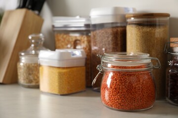 Different types of cereals and legumes in containers on light table, closeup