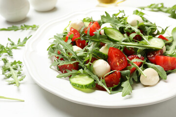 Tasty salad with arugula, mozzarella, tomatoes and cucumber on white table, closeup