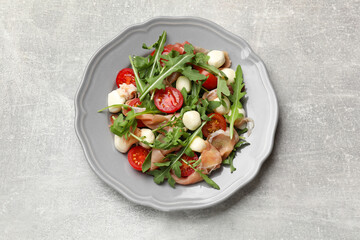 Tasty salad with arugula on grey textured table, top view