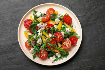 Tasty salad with arugula, cheese and vegetables on dark textured table, top view