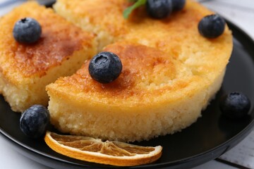 Delicious semolina cake with blueberries and orange slices on white wooden table, closeup