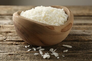 White soy wax flakes in bowl on wooden table, closeup
