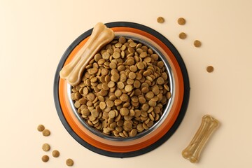 Dry pet food in feeding bowl and chew bones on beige background, top view