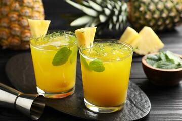 Tasty pineapple cocktail with mint in glasses and jigger on black wooden table, closeup