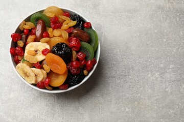 Mix of different dried fruits in bowl on gray textured table, top view. Space for text