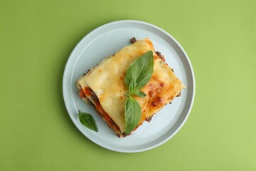 Delicious cooked lasagna with basil on light green table, top view