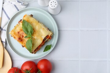 Delicious cooked lasagna with basil served on white tiled table, flat lay. Space for text