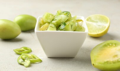 Delicious salsa (Pico de gallo) in bowl and products on light textured table, closeup