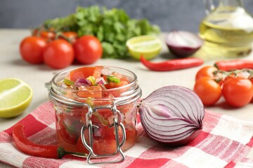 Delicious salsa (Pico de gallo) in jar and ingredients on light table, closeup