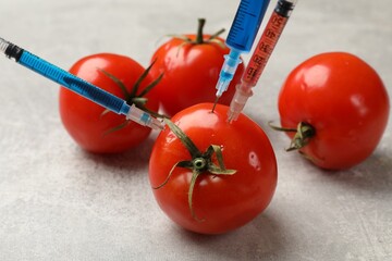 GMO concept. Tomato with different syringes on grey textured table, closeup