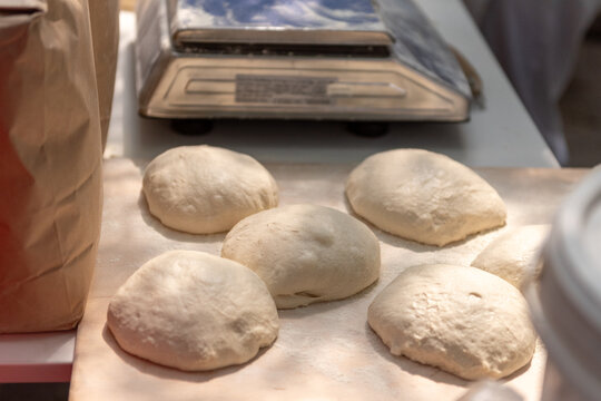 Balls of fresh homemade dough on floured wooden board.
