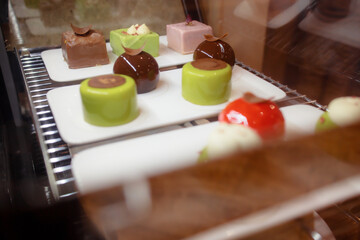 Delicious soft desserts on display. A variety of chocolate cakes in the refrigerator. Close-up view of a delicious Asian cake. Signature ice cream on disposable tableware. Green, red and brown cakes.