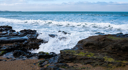 Obraz premium Waves breaking on coastal rocks beach in new zealand