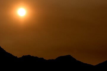 Sun shining through hazy sky and silhouette of mountain