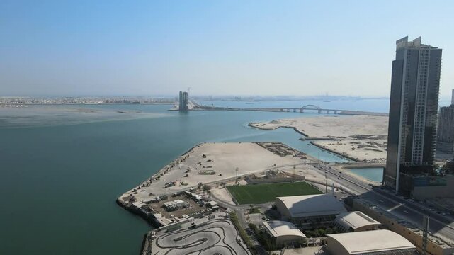 A camera drone fies ahead over the Al Najmah Club sports center, Juffair Beach towards Prince Khalifa bin Salman Bridge, Manama, Bahrain