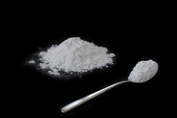 Spoon and pile of flour on black background